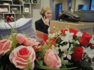 Accueil téléphonique dans une agence funéraire avec arrangement floral au premier plan.