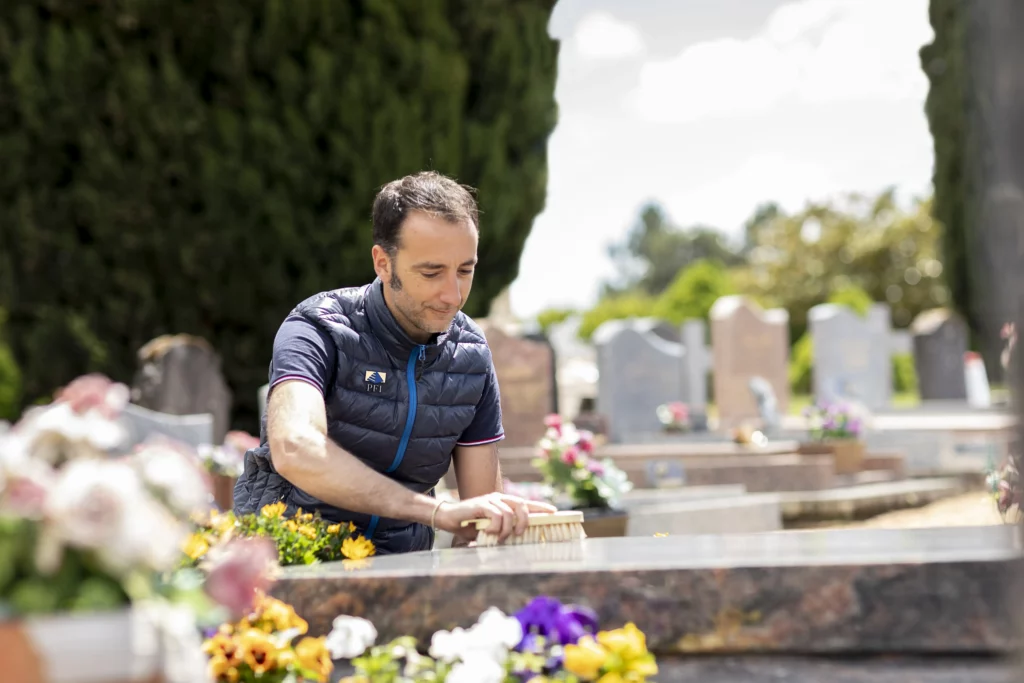 Agent des pompes funèbres nettoyant et entretenant une tombe dans un cimetière.